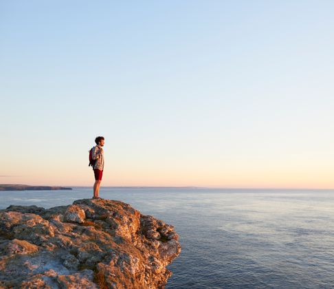 A male hiker looks towards the sunset from an Atlantic cliff.