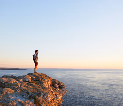 A male hiker looks towards the sunset from an Atlantic cliff.