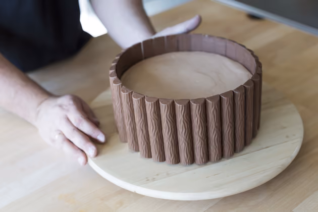 Am Ende müssen die Pralinen etwas versetzt angelegt werden, damit die Torte ganz bedeckt ist. Ein dekoratives Band hält die Pralinen zusätzlich fest.