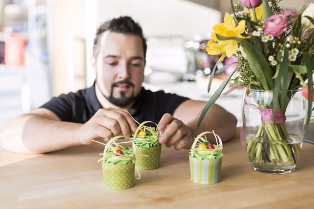 Buntes Papier in 1cm Streifen schneiden. Den gebackenen Muffin mit einem Messer vom Rand lockern und das Papier auf zwei Seiten hineinstecken. Am Ende drei bunte Schokoeier drappieren.