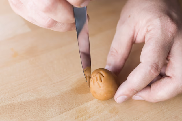Die größere und mittlere Kugel leicht konisch oder spitz zulaufend formen. Die größere ist der Körper des Hasen. Die mittlere wird zu seinem Schwanz. Nach dem Formen den Schwanz mit der Rückseite eines Messers "Haare" verpassen. Dabei das Marzipan leicht einritzen.
