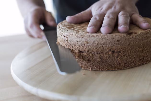 Der erste Trick von Moschen: Um die Torte in die Hälfte zu schneiden, mit einem Messer die Mitte zunächst nur einritzen und nach und nach tiefer in die Torte schneiden, so werden die Hälften gerade. Die Torte am besten auf ein Drehteller schneiden. Mit einer Hand die Torte leicht fixieren. Die Torte kann natürlich auch gedrittelt werden.