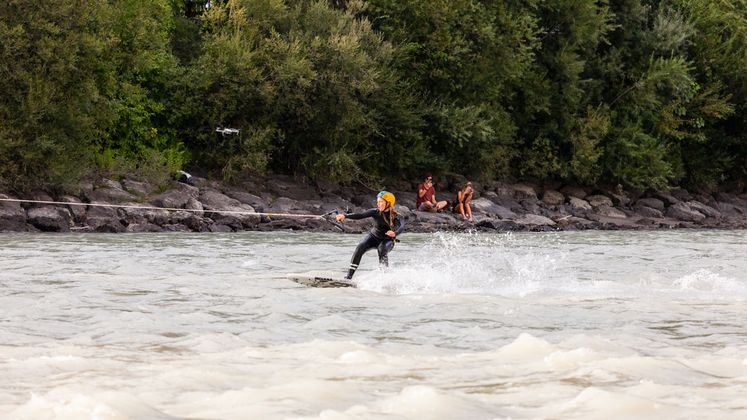 Der Surfer hält ein Seil fest, das über Umlenk­rollen an einer Brücke mit einem „Unterwassersegel“ verbunden ist.