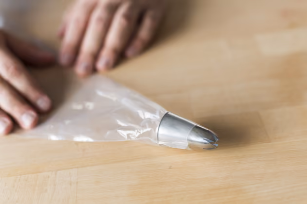 Um die Creme aufzuspritzen, einen Plastik-Spritzbeutel am spitzen Ende ein wenig abschneiden und eine größere Tülle von innen durchdrücken.