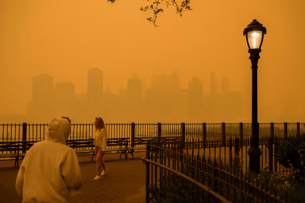 The skyline of lower Manhattan is seen past pedestrians as smoke from wildfires in Canada cause hazy conditions in New York City on June 7, 2023. An orange-tinged smog caused by Canada's wildfires shrouded New York on Wednesday, obscuring its famous skyscrapers and causing residents to don face masks, as cities along the US East Coast issued air quality alerts. (Photo by ANGELA WEISS / AFP)